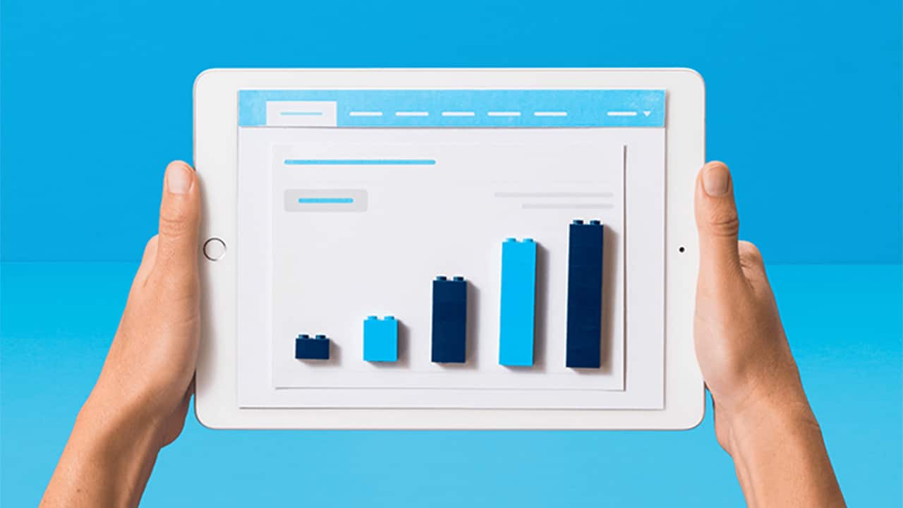 A hand holding a tablet with a lego graph representing a report